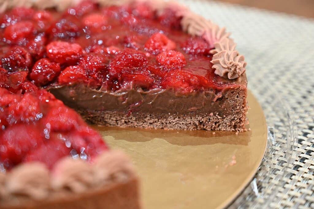 Side close up image of the whole Costco Kirkland Signature Chocolate Raspberry tart with a slice taken out  the so you can see the distinct layers. 