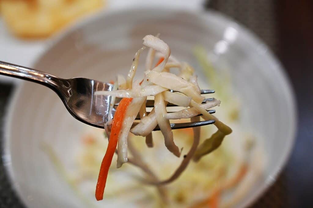 Close up image of the Costco Kirkland Signature Fish & Chips Meal Kit slaw on a fork with a bowl of slaw in the background