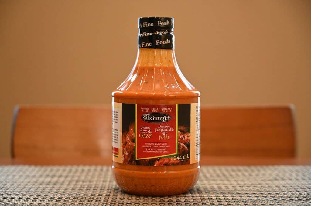 Costco Johnny's Sweet, Hot & Crazy Marinade and Wing Sauce bottle sitting on a table, sideview image. 