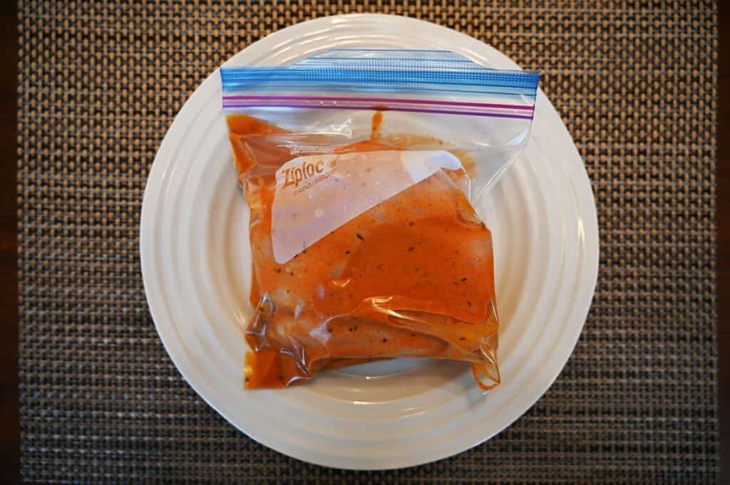 A ziplock bag of chicken on a white plate with Costco Johnny's Sweet, Hot & Crazy Marinade and Wing Sauce poured into the bag as a marinade. 