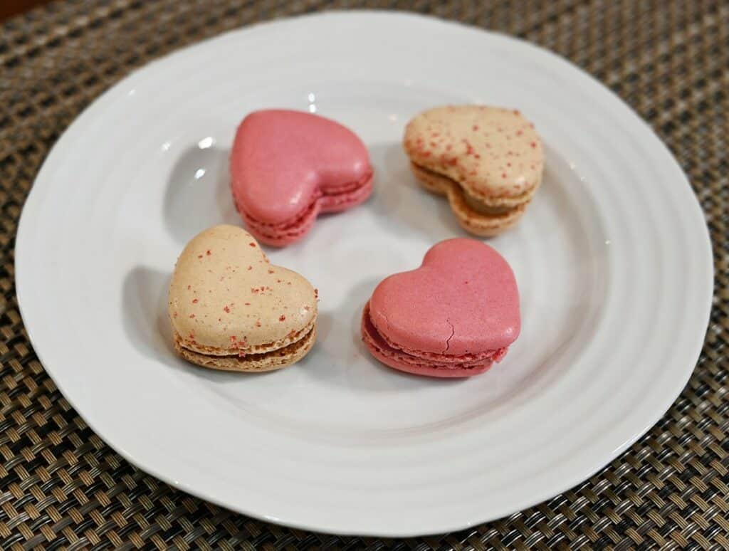 Four Costco Le Bon Patisserie Heart Shaped Macarons on a white plate, two raspberry and two vanilla. 