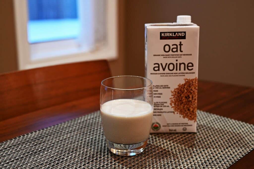 Costco Kirkland Signature Organic Oat Beverage poured into a glass with the container beside the glass, on a table. 