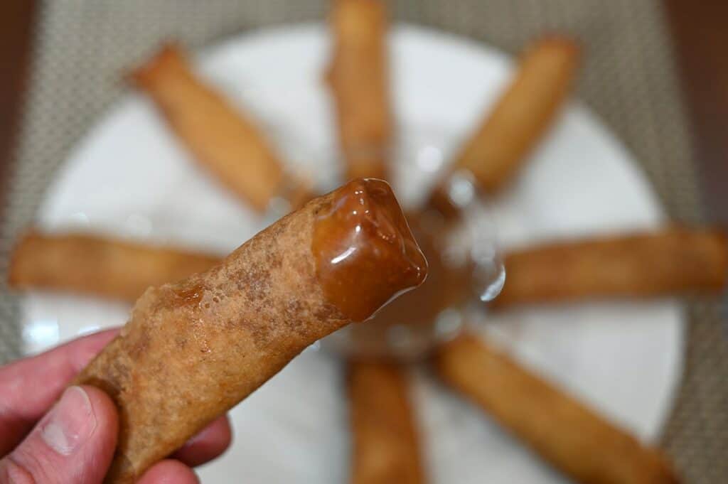 Close up image of one Costco Summ! Apple Pie Roll dipped in caramel sauce. 