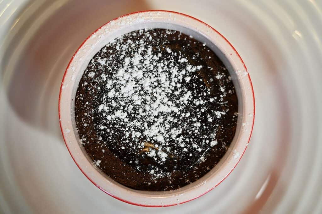 Closeup image of the top of a heated Costco Delici Belgian Chocolate Soufflé with icing sugar dusted on top and on a white plate after heating.
