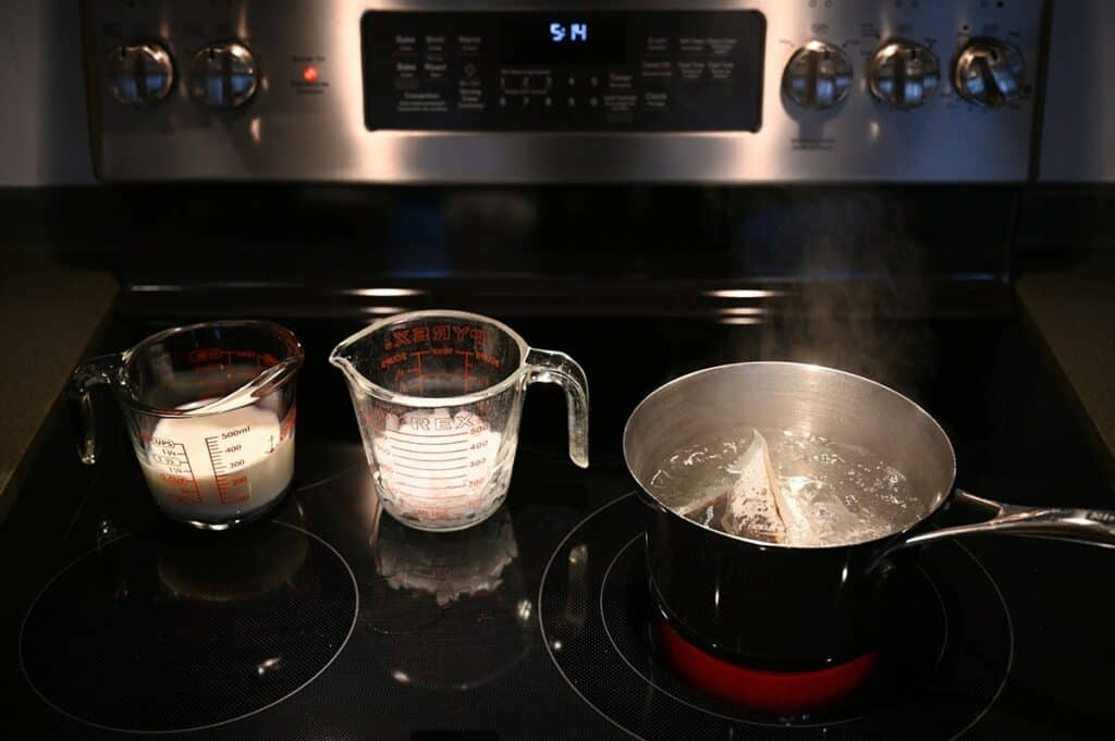 Making the Costco Boba Bam Instant Boba using the stove top method, showing a measuring cup with milk, ice and a boba packet boiling in a pot of water. 