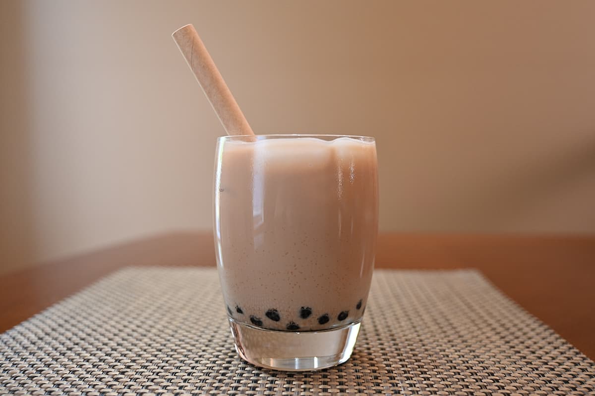 Image of a clear glass filled with prepared milk tea boba with a paper straw in the glass.