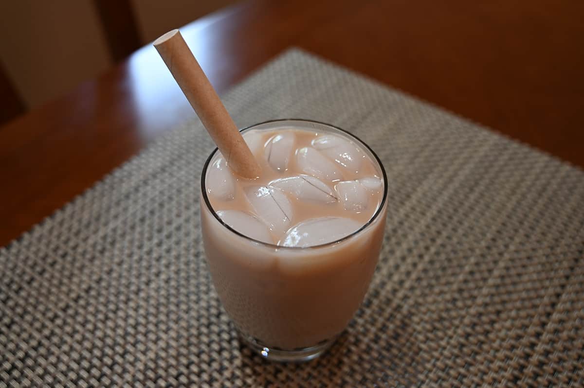 Top down image of the milk tea prepared in a glass with lots of ice in it and a paper straw. The glass is sitting on a table.