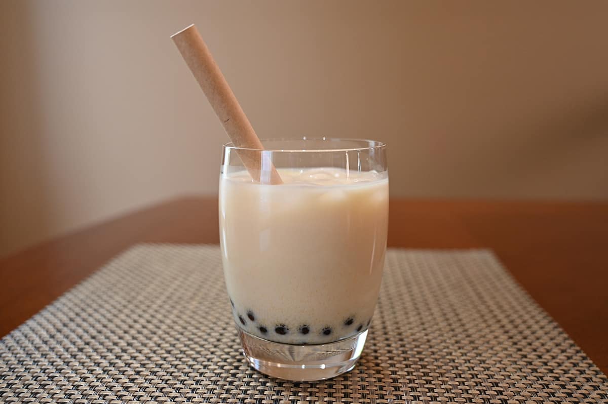 Image of a clear glass prepared and filled with mango boba and ice. There's a paper straw inside the glass.