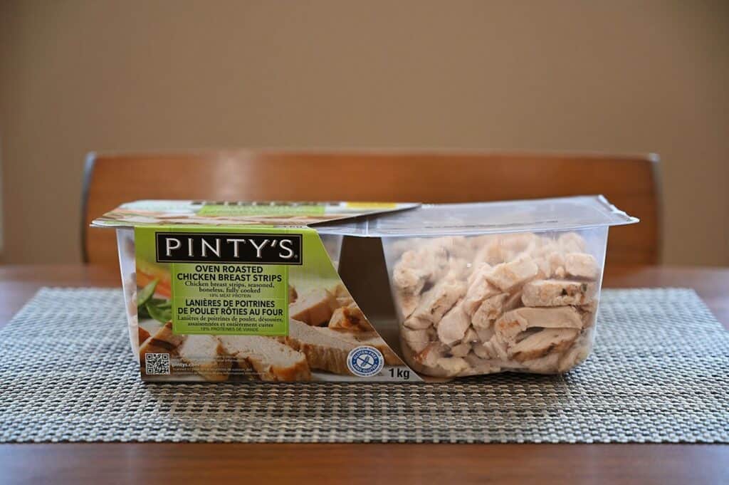 Costco Pinty's Oven Roasted Chicken Breast Strips packaging on a grey placement on a wood table. Sideview image.