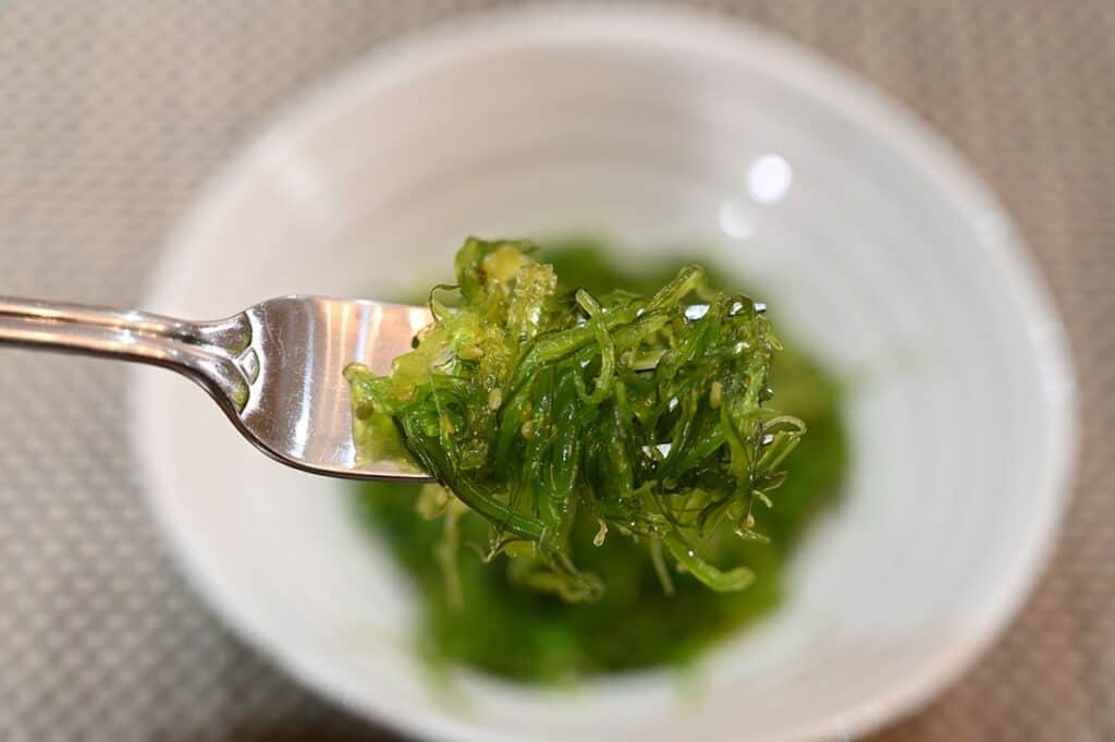 Costco Azuma Seaweed Salad served in a white bowl, closeup image of the seaweed salad on a fork. 
