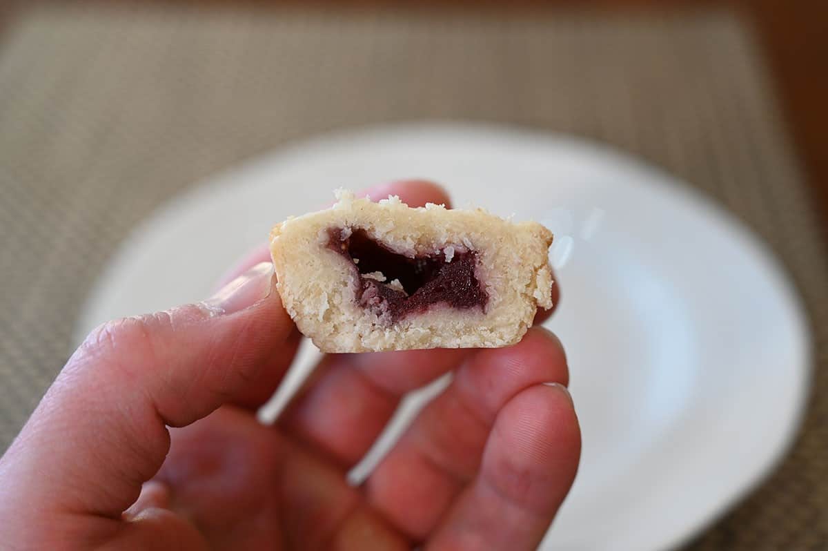 Closeup image of one bite with a bite taken out of it to show the raspberry filling in the middle. 
