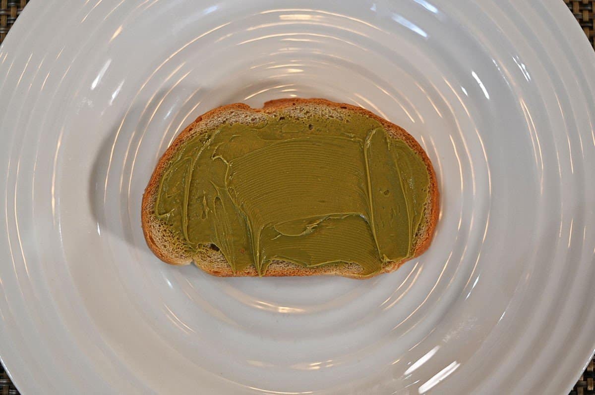 Costco Pisti Spreadable Pistachio Cream spread on a slice of toast and served on a white plate. 