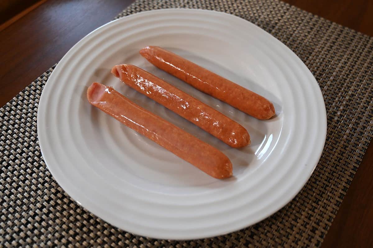 Three Costco Siwin Japanese Style Sausages  on a white plate before cooking. 