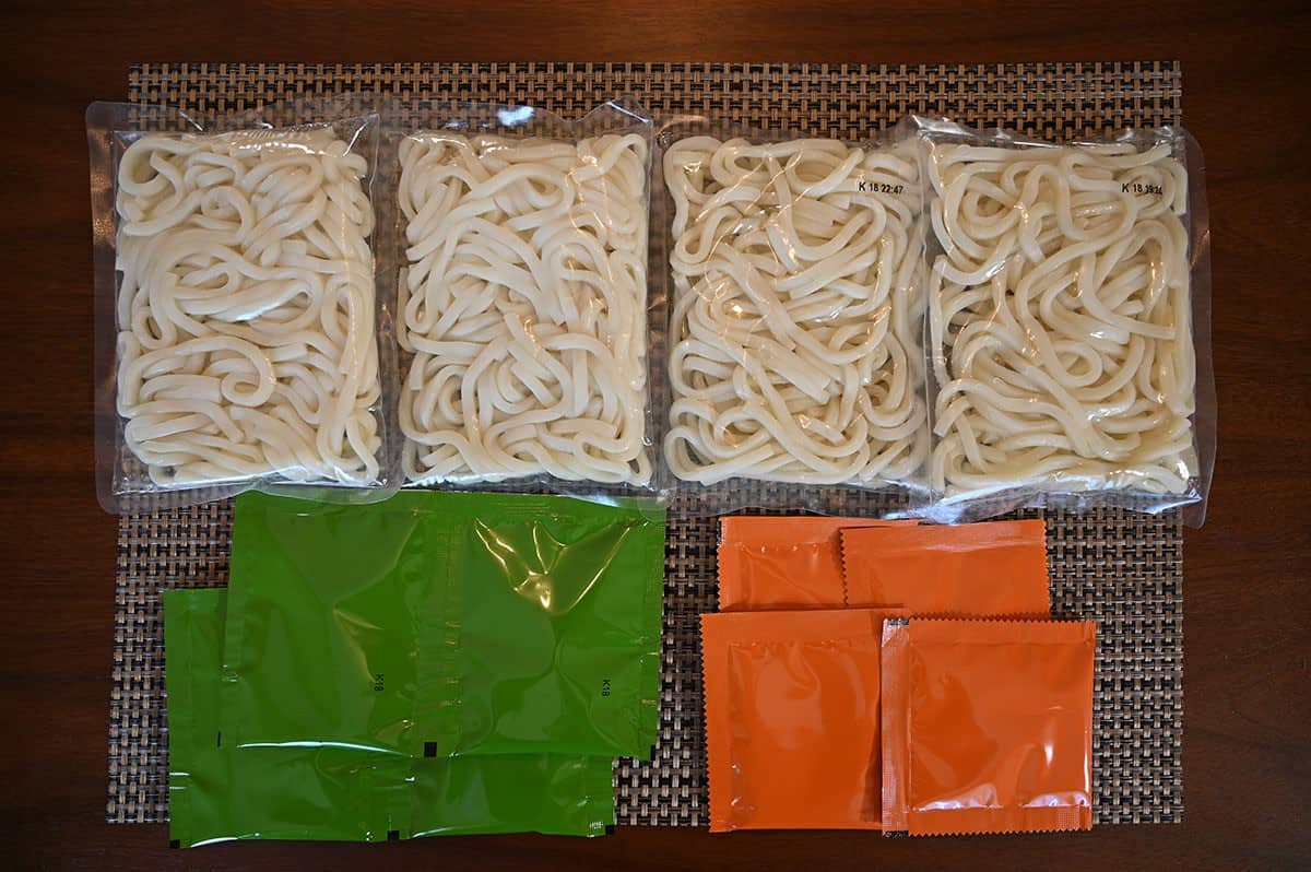 All the contents of the Costco Pulmuone Stir-Fry on a table laid out, four noodles, four orange packets of seasoning and four green packets of vegetables. 