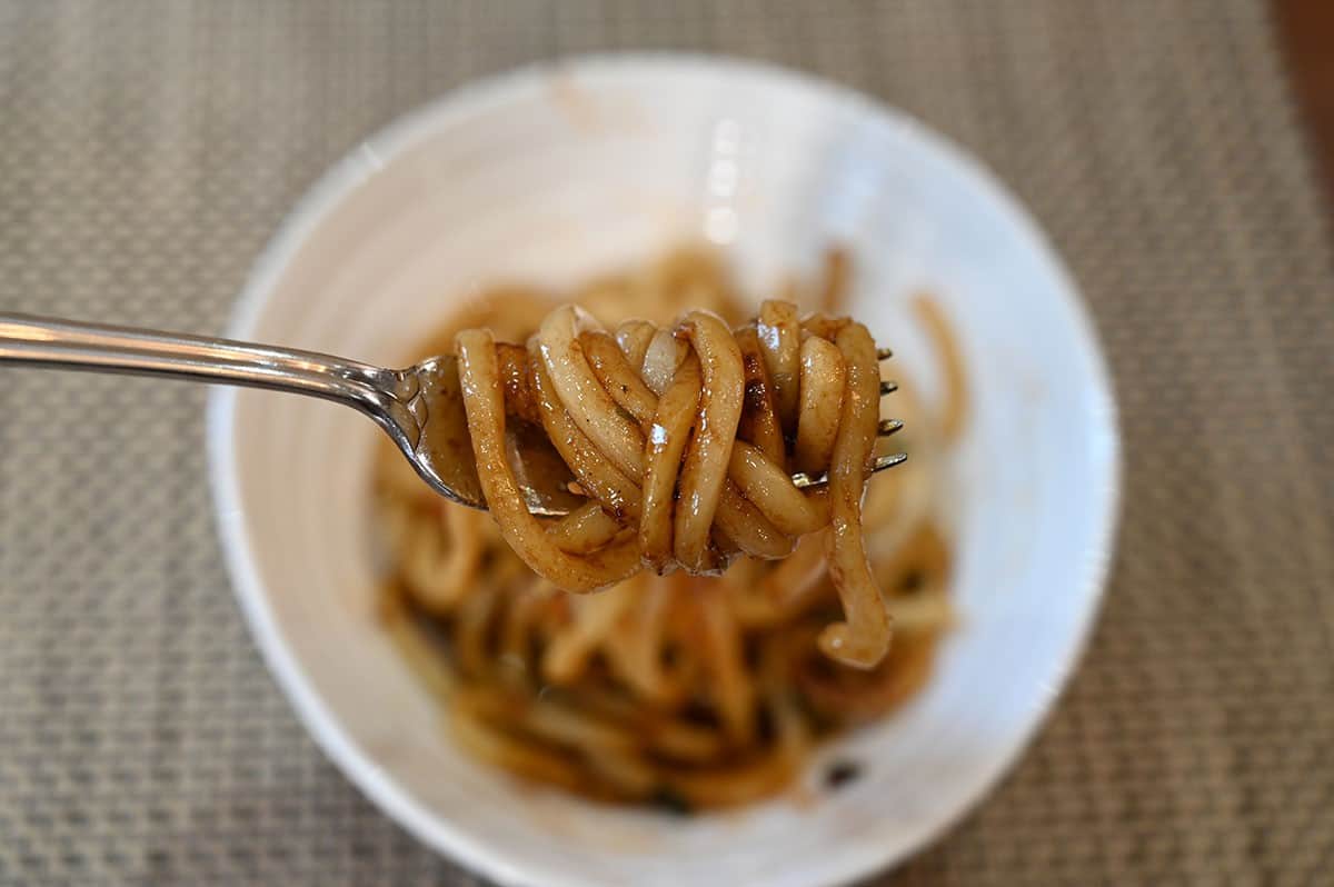 Costco Pulmuone Teriyaki Stir-Fry Udon cooked and served in a white bowl, closeup image of noodles wrapped around a fork. 