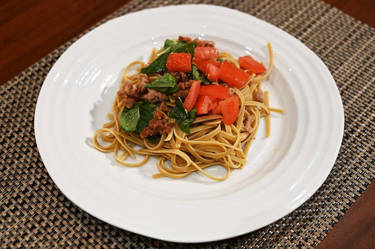 Image of Costco Pedon Four Bean Linguini prepared with basil and tomatoes on a white plate, sitting on a table. 