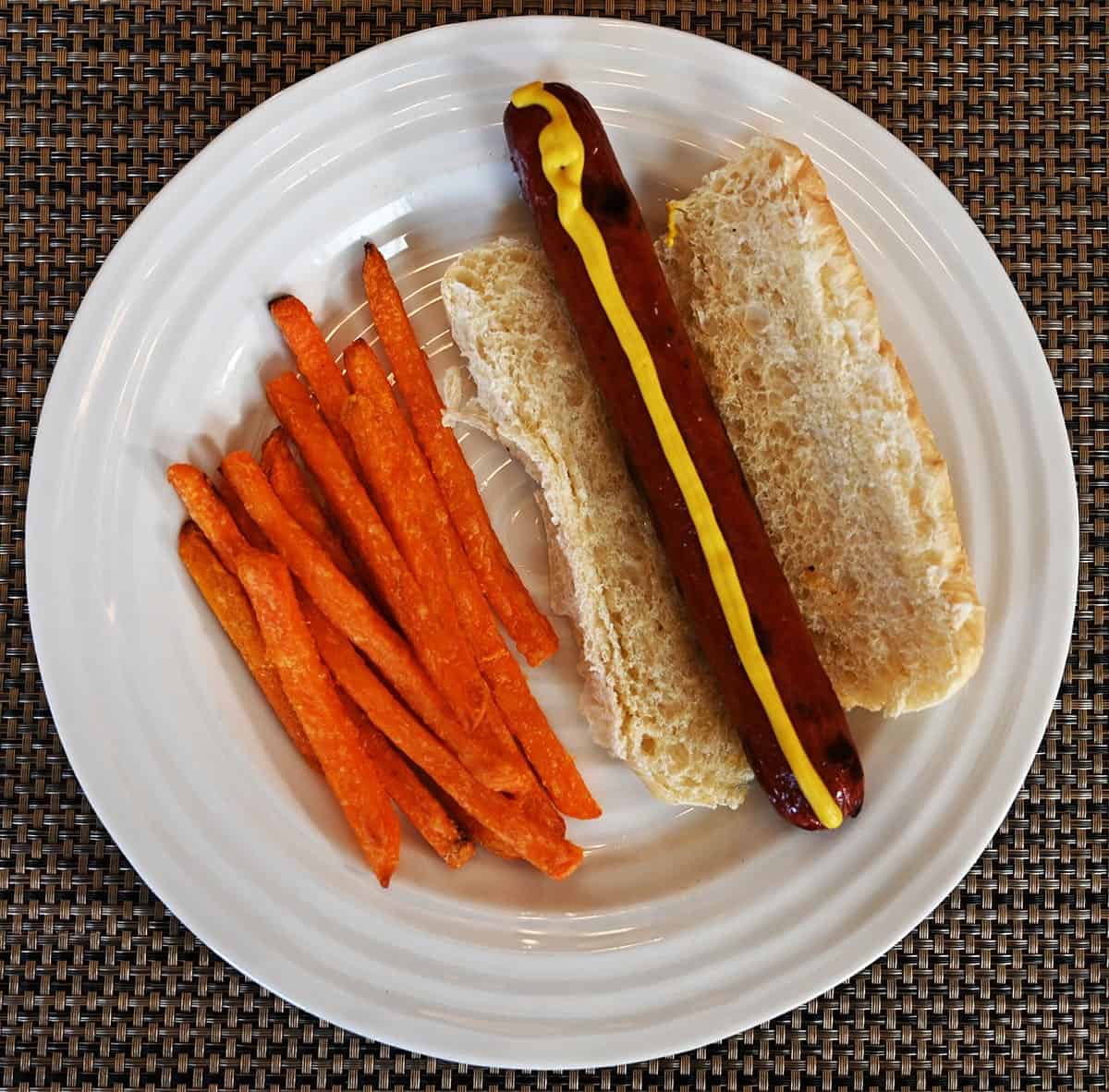 Cooked Costco Polish Sausage on a bun with sweet potato fries beside it served on a white plate. 