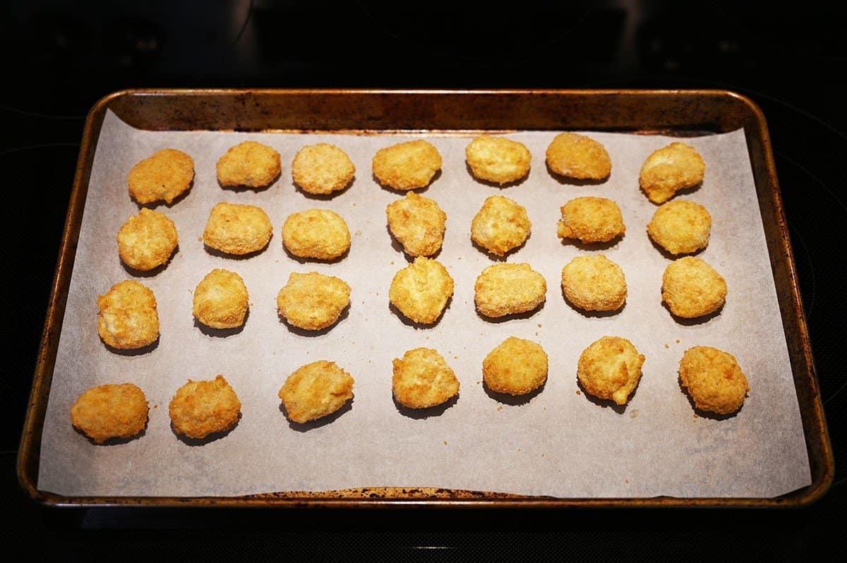 Costco Hampton House Popcorn Chicken spread out on a baking tray lined with parchment paper, in the oven. 