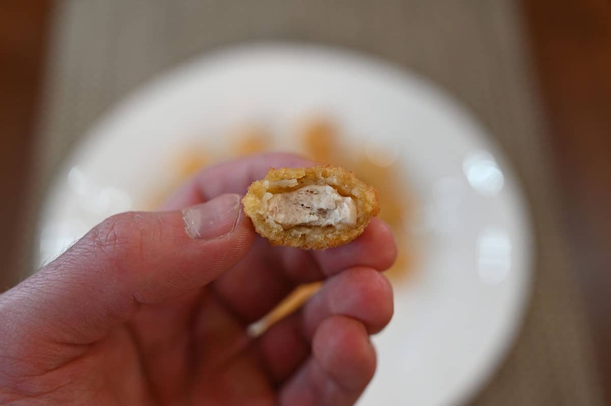 Image of one piece of popcorn chicken with a bite taken out of it so you can see the middle. 