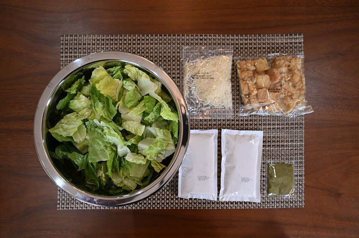 All the contents of the Costco Taylor Farms Ultimate Caesar Salad Kit laid out on a table, top down image. 