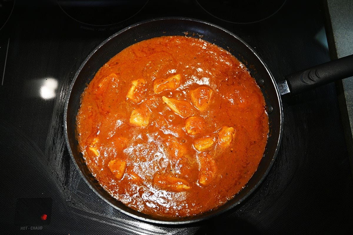 Chicken vindaloo simmering in sauce in a pan on the stove.