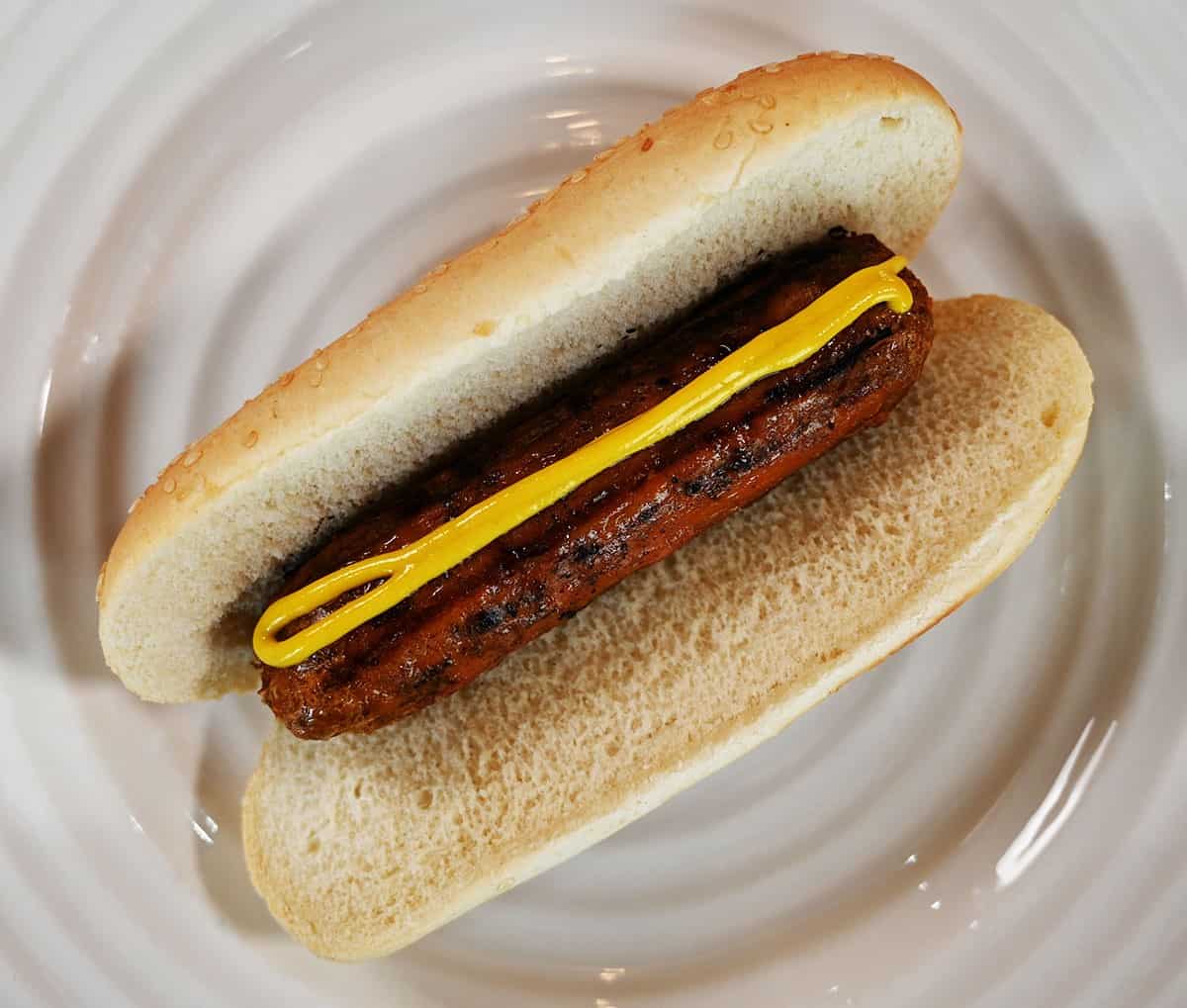 Costco Beyond Meat Beyond Sausage served like a hot dog with mustard on it, on a white plate. 