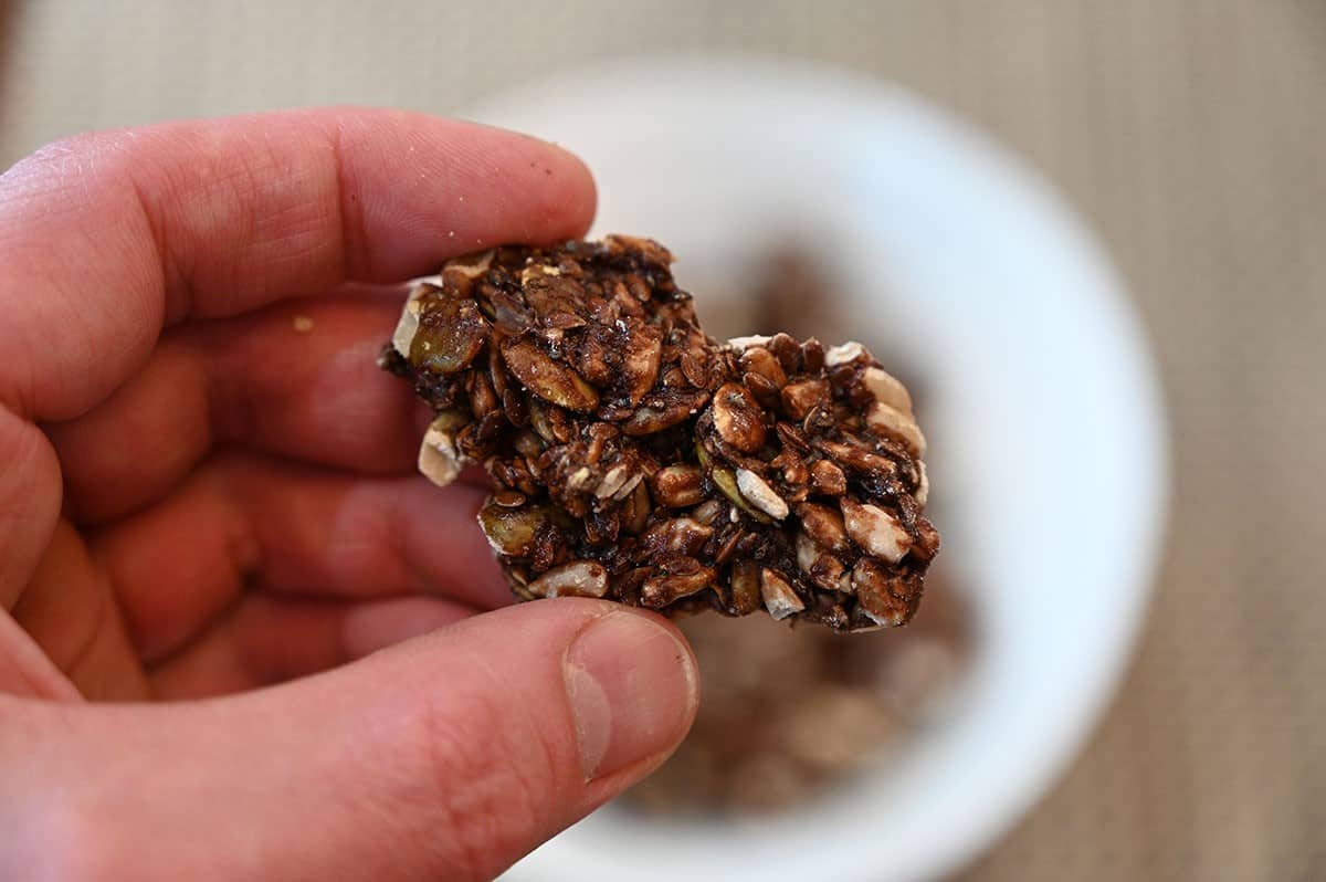 Closeup image of one keto cluster being held with the bowl of clusters in the background. 