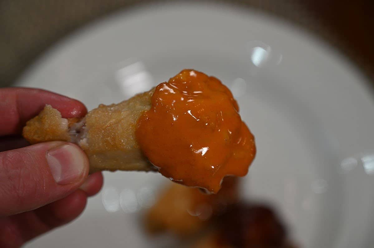 One Costco Pinty's Crispy Chicken Wing dipped in buffalo sauce, closeup image. 