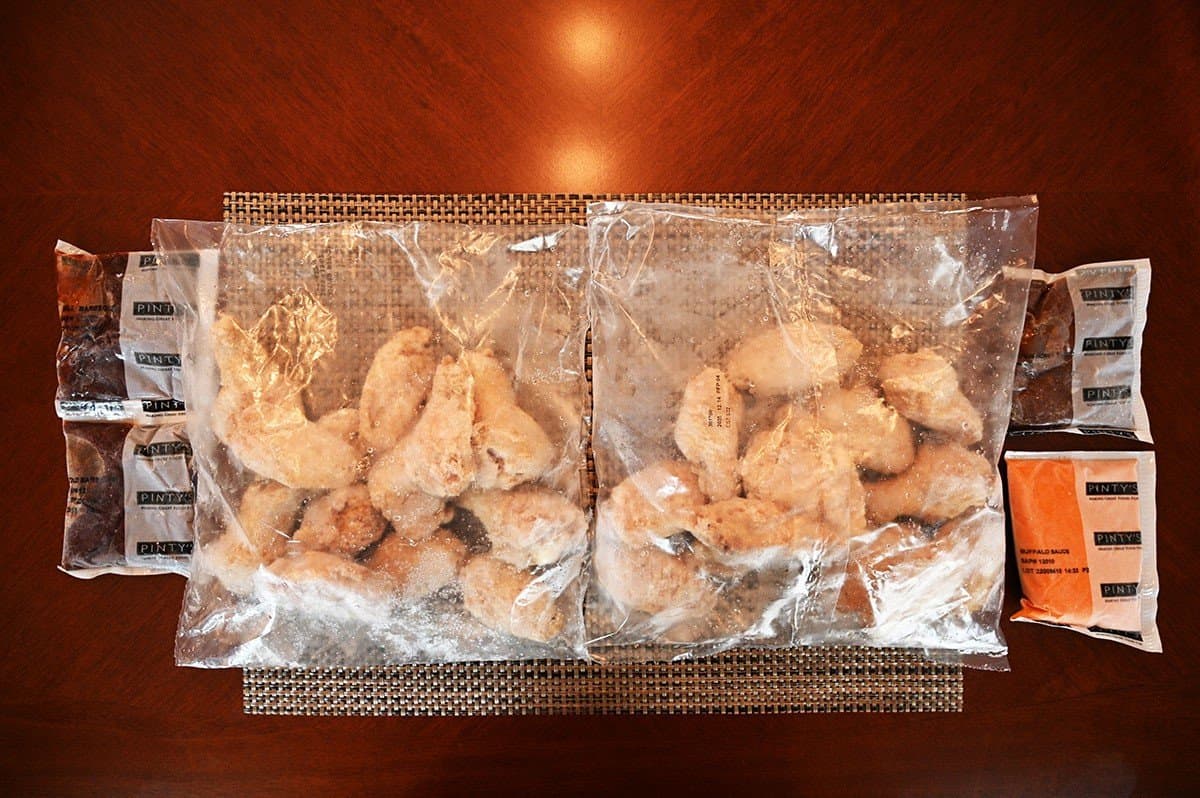 Image of two bags of wings and four sauces that come in the box of wings on a table. 
