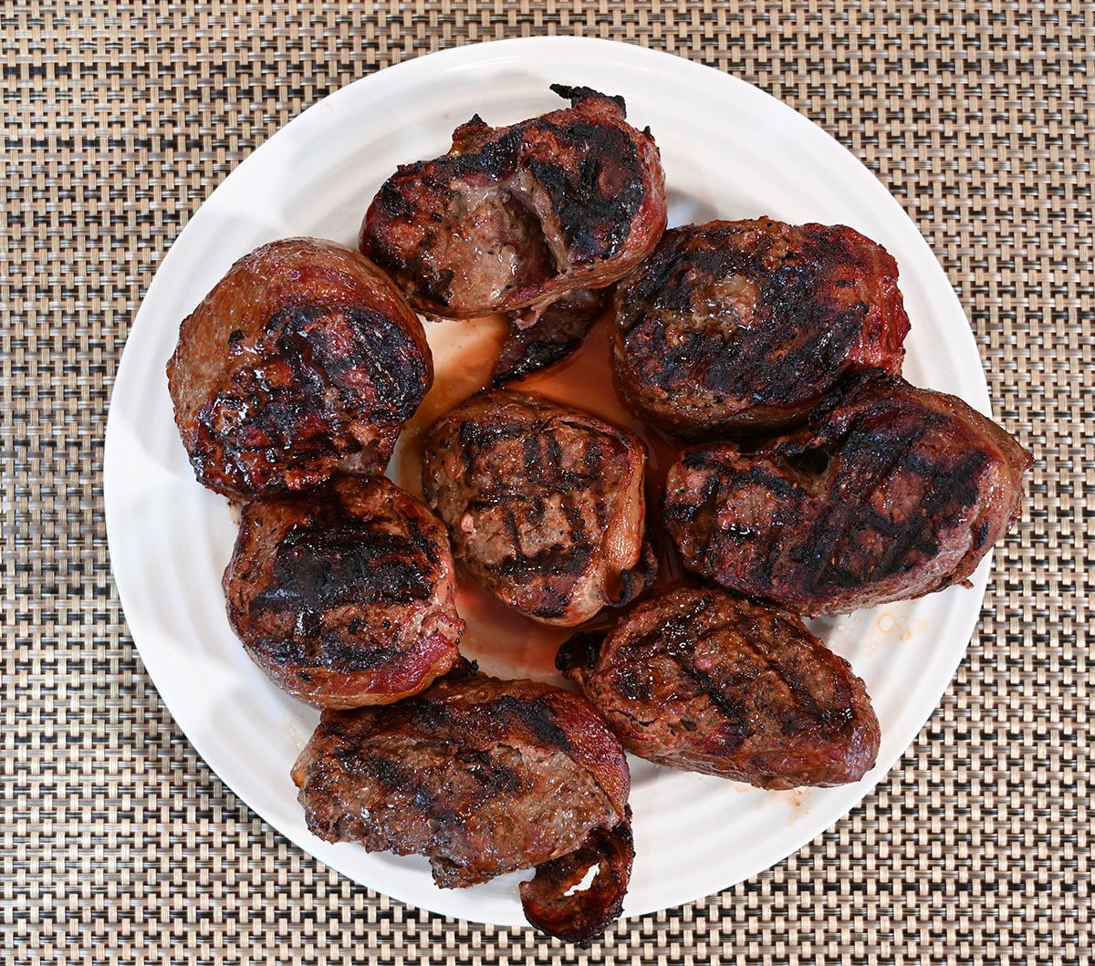 Closeup top down image of eight beef tournedos cooked and on a white plate. 