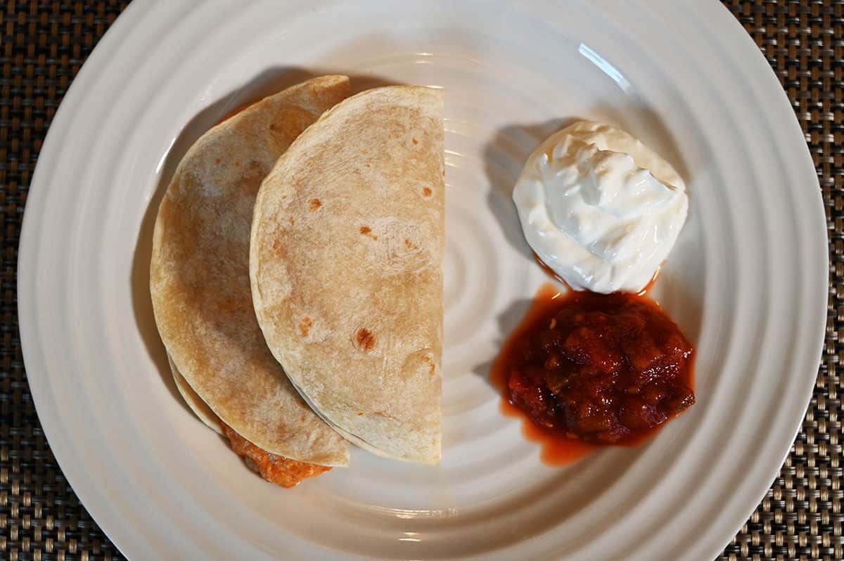 Image of two Costco Catarina Chicken Quesadillas cooked and served on a white plate with salsa and sour cream beside the quesadillas.