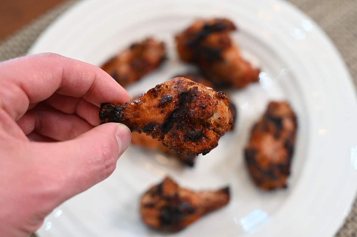 Close up image of one Costco chicken wing drumstick grilled with white plate containing other chicken wings in the backfround. 