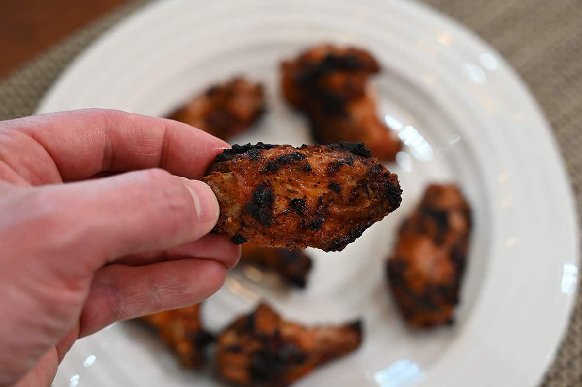 Close up image of one Costco chicken wing grilled with white plate containing other chicken wings in the backfround. 