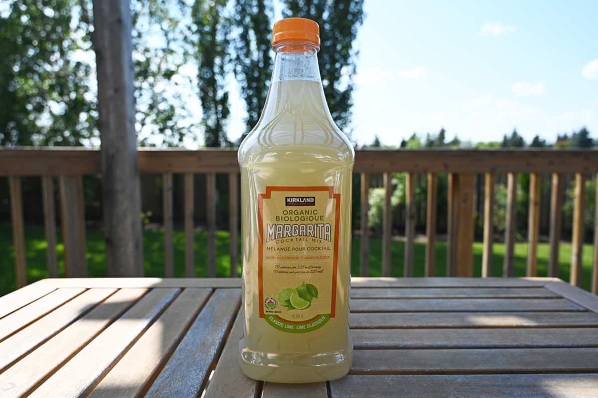 Image of the Costco Kirkland Signature Organic Margarita Mix bottle sitting on a deck outside with grass and trees in the background.