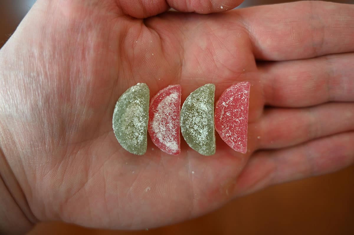 Four sourmelon bites, closeup image of two green and two pink in the palm of a hand.