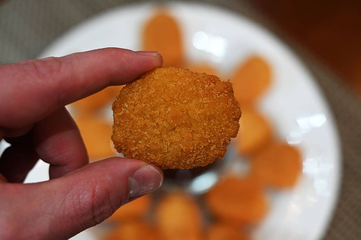 Closeup image of one chicken nugget with a plate of chicken nuggets in the background.