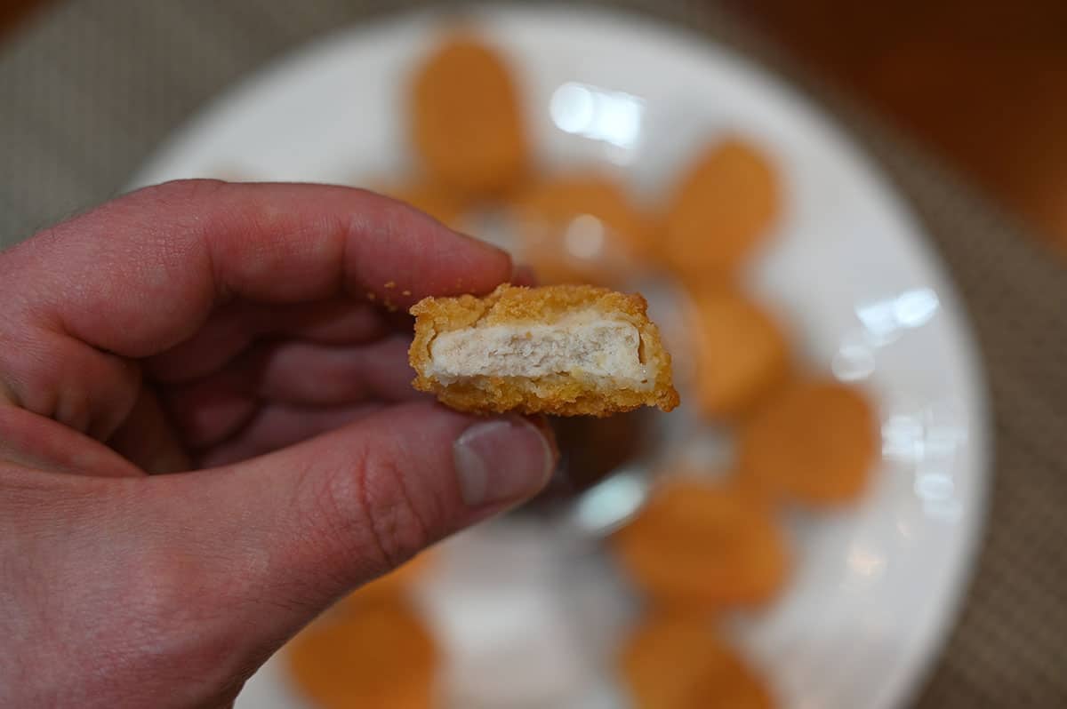 Closeup image of the inside of one chicken nugget, cooked. White plate with chicken nuggets on it in the background.