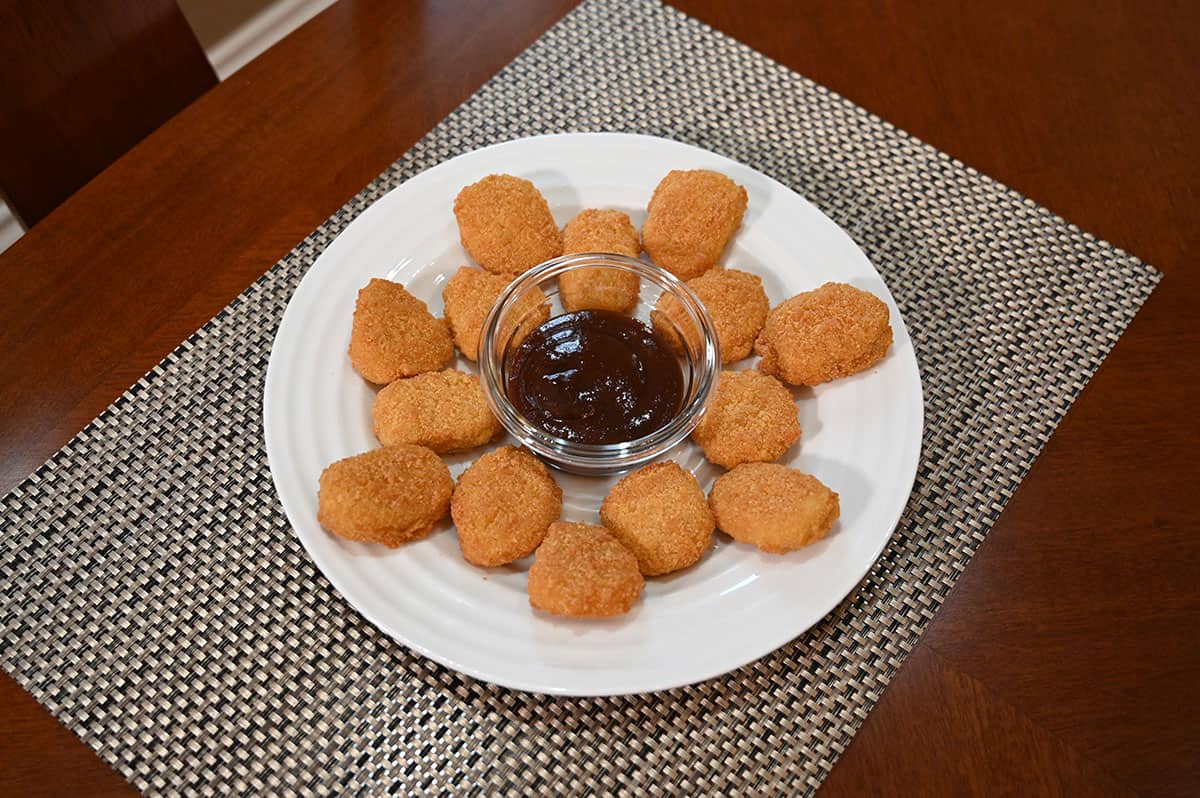 White plate with chicken nuggets on it and a dipping sauce in a bowl in the middle.