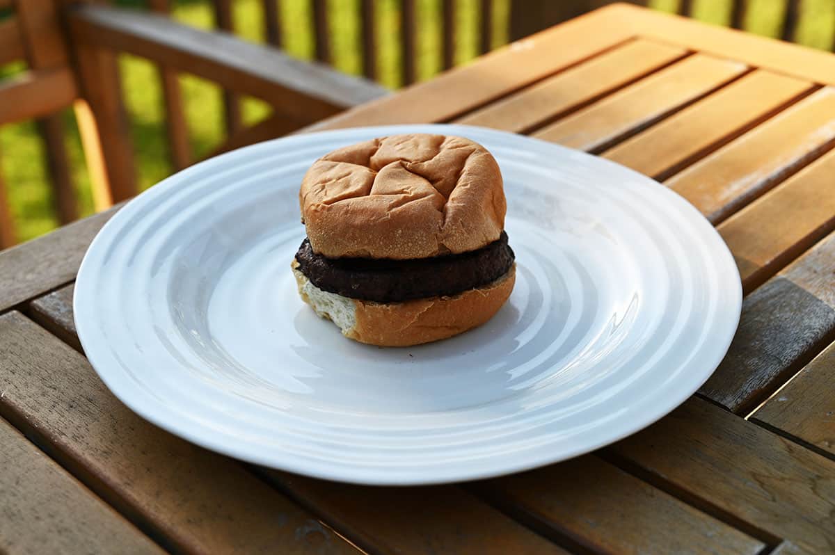 Image of a cooked veggie burger in a bun on a white plate on a table outside. 