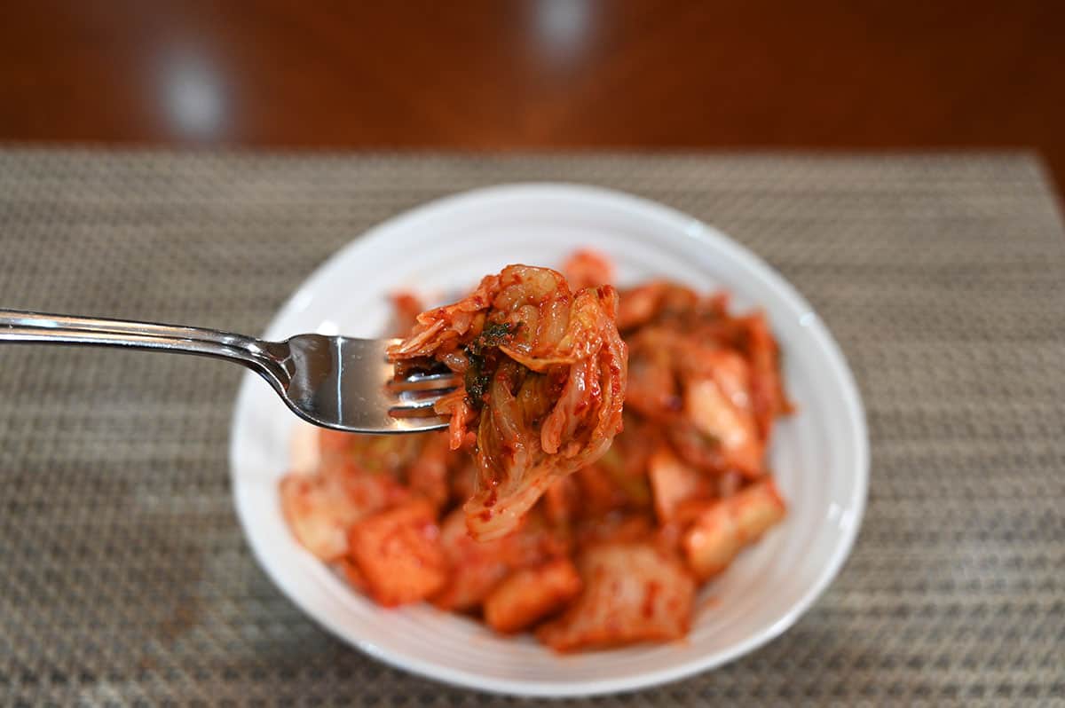 Forkful of kimchi with a bowl of kimchi in the background.