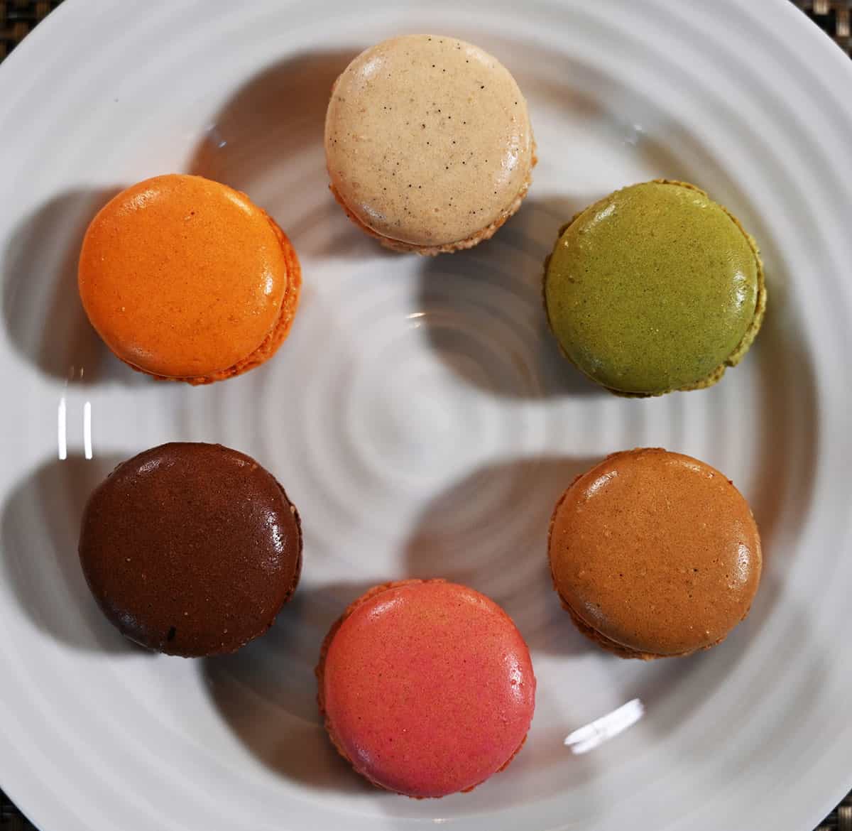 Image of all six flavors of macarons on a white plate laid out in a circle. top down closeup image.