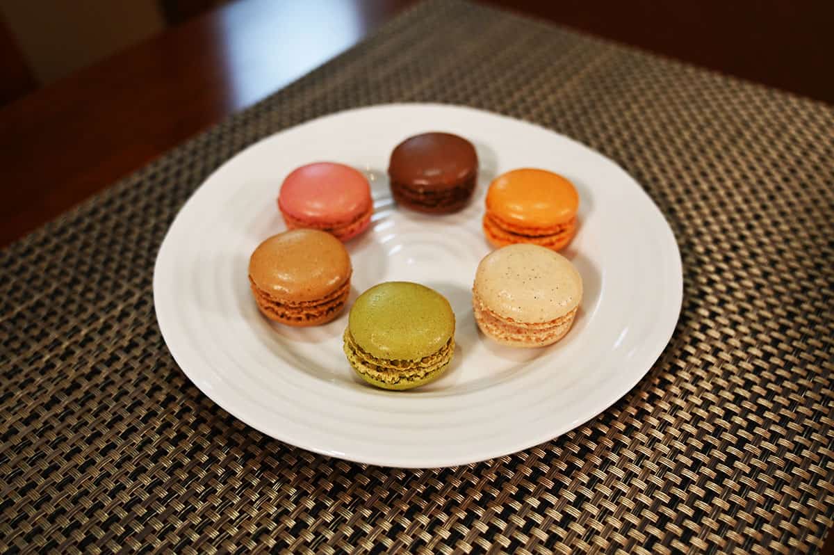 Image of all six flavors of macarons on a white plate laid out in a circle. 
