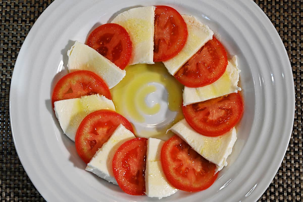 Image of a carprese salad on a white plate - slices of mozzarella and tomato with olive oil drizzled on top.