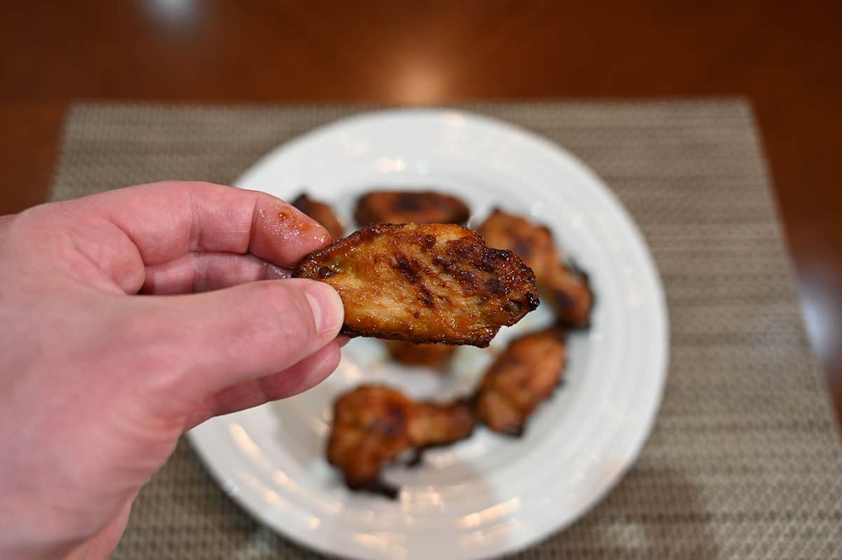 Closeup image of one chicken wing with plate of wings behind it in the background.