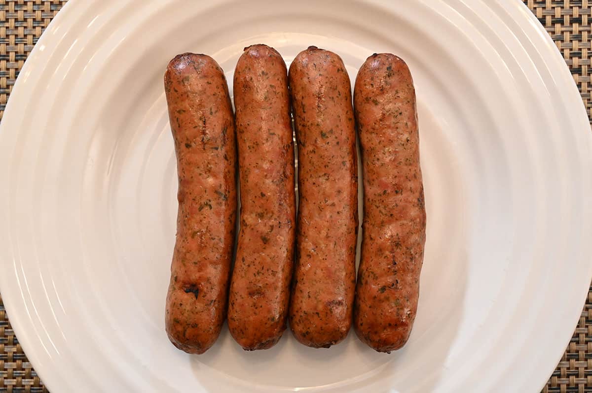 Image of four uncooked chicken sausages lined up on a plate.