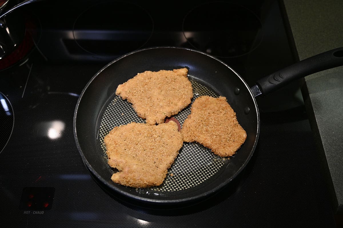 Three pieces of frozen schnitzel cooking in a pan.