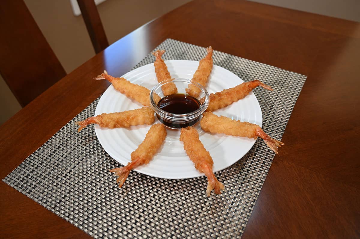 A plate of eight tempura shrimp with a bowl of dipping sauce in the middle.