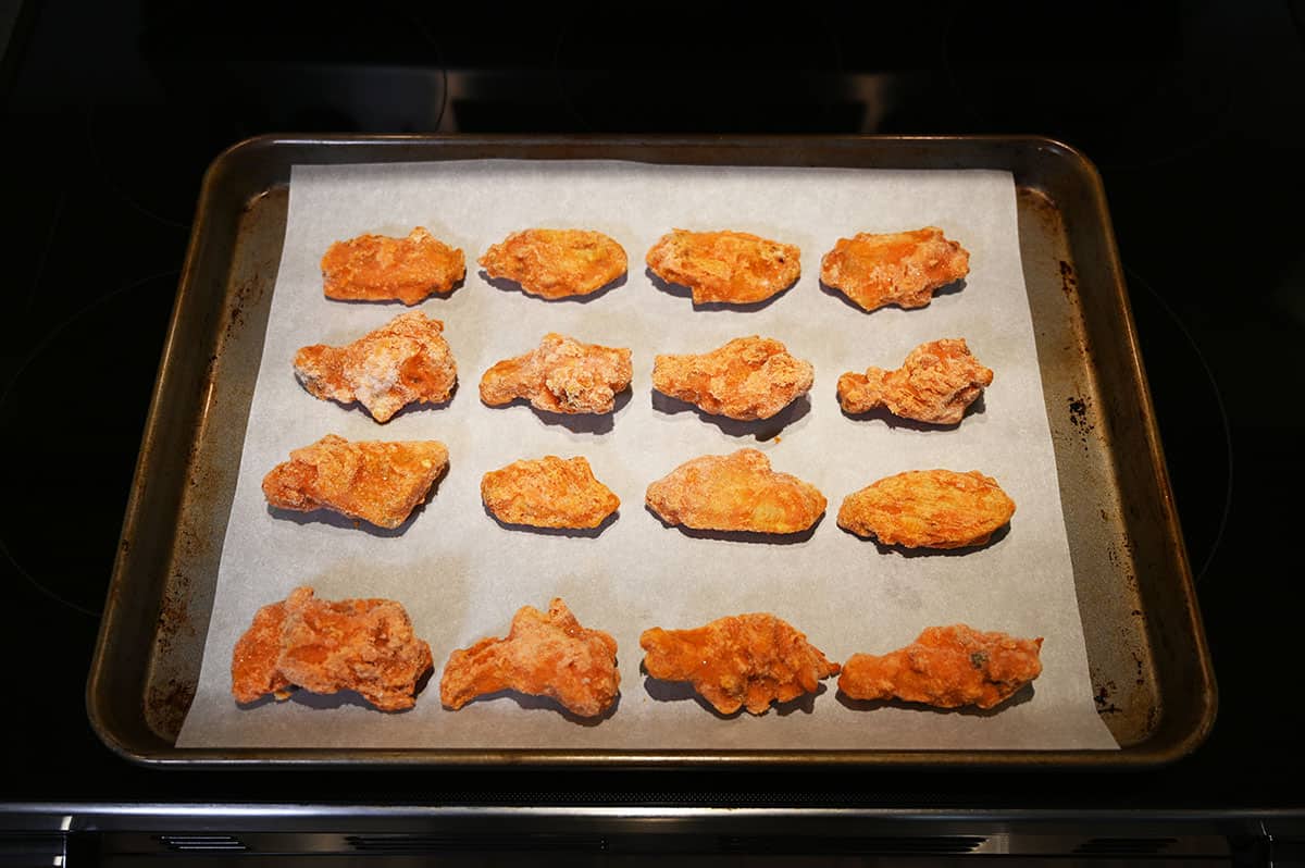Cookie tray with chicken wings on it cooking in the oven.
