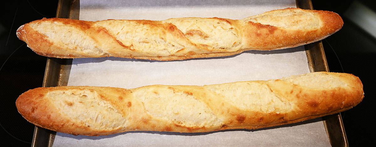 Image if two garlic baguettes on a cookie sheet with parchment paper on the cookie sheet. Prior to baking.