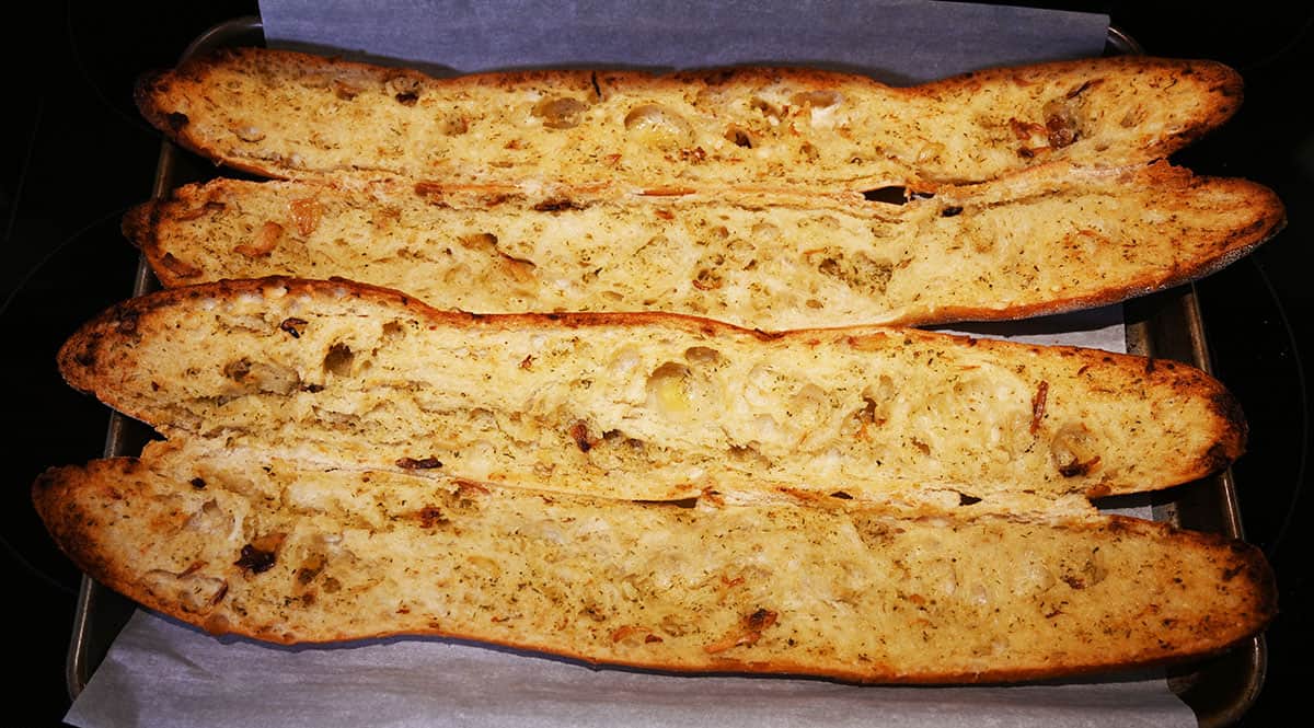 Image if two garlic baguettes on a cookie sheet with parchment paper on the cookie sheet after baking, opened.